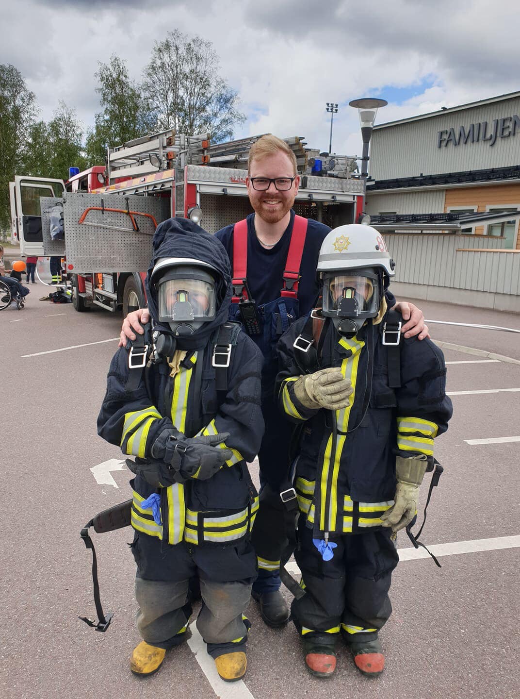 Syntolkning av bild: Brandman som håller om två barn som är iklädda larmställ