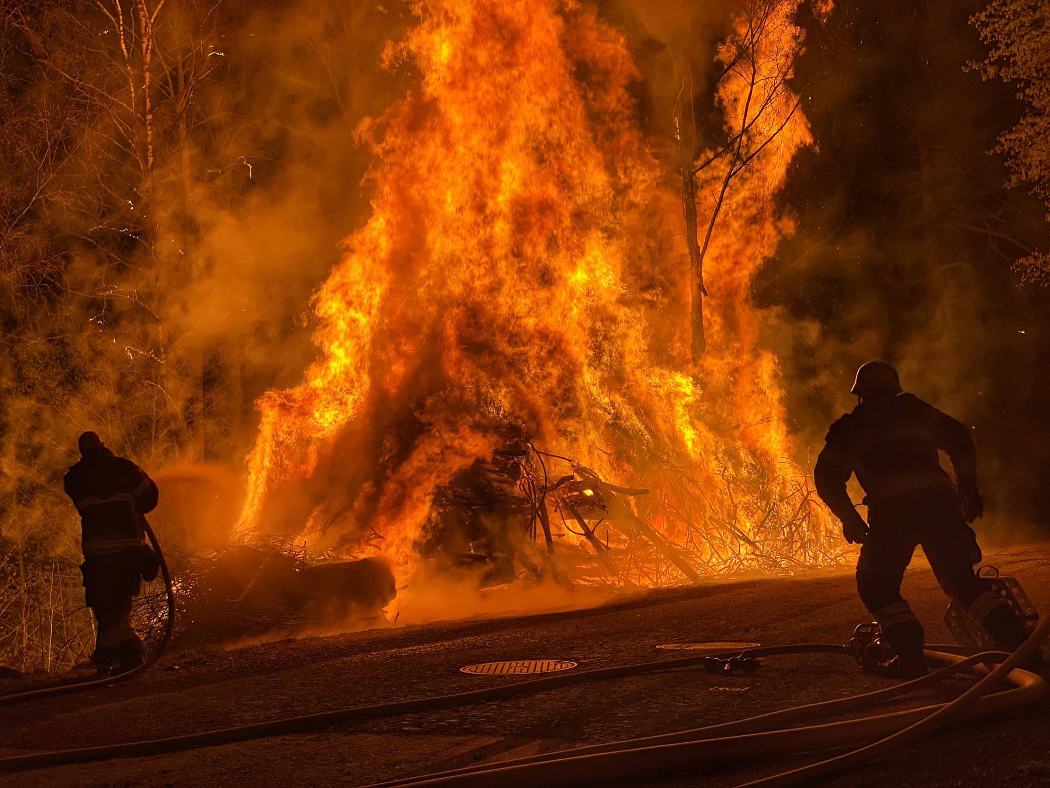 Syntolkning av bild: Brandmän släcker en brinnande rishög
